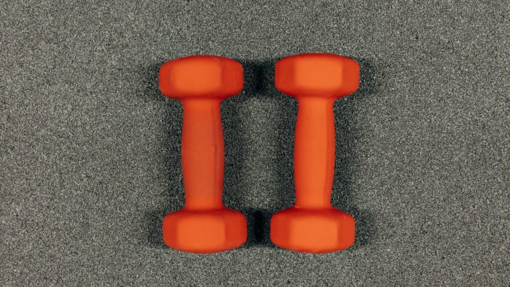 Orange dumbbells on a gray surface, symbolizing care for the body through daily practice.