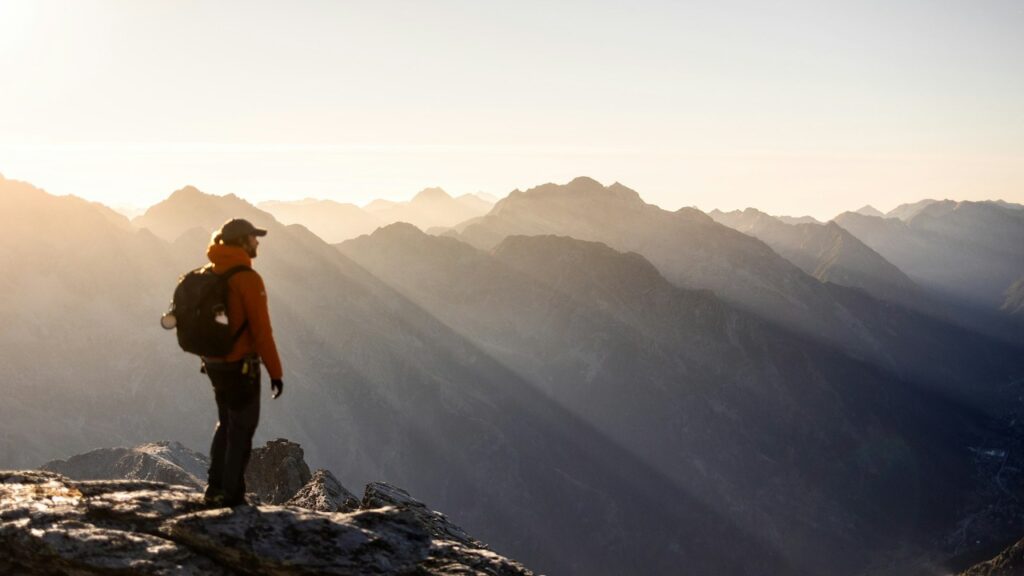 A hiker standing on a mountain summit at sunrise, symbolizing inner courage and self-mastery.